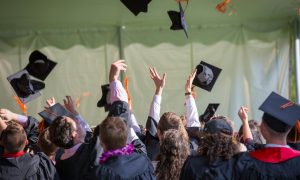 Group of graduates celebrating by tossing caps into the air during a graduation ceremony.
